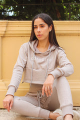 Woman Sitting in Grey French Terry Drawstring  Hoodie and Pant Set with cafecito screen  next to a yellow wall and tree